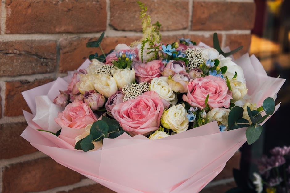 A bouquet arrangement featuring pink roses, white eustoma, small white baby's breath, and sprigs of green eucalyptus, wrapped in soft pink tissue paper. The flowers are fresh with slightly ruffled pet
